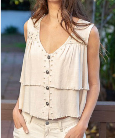 A sleeveless beige top with buttons down the center, a v-neck, and ruffle detailing. 