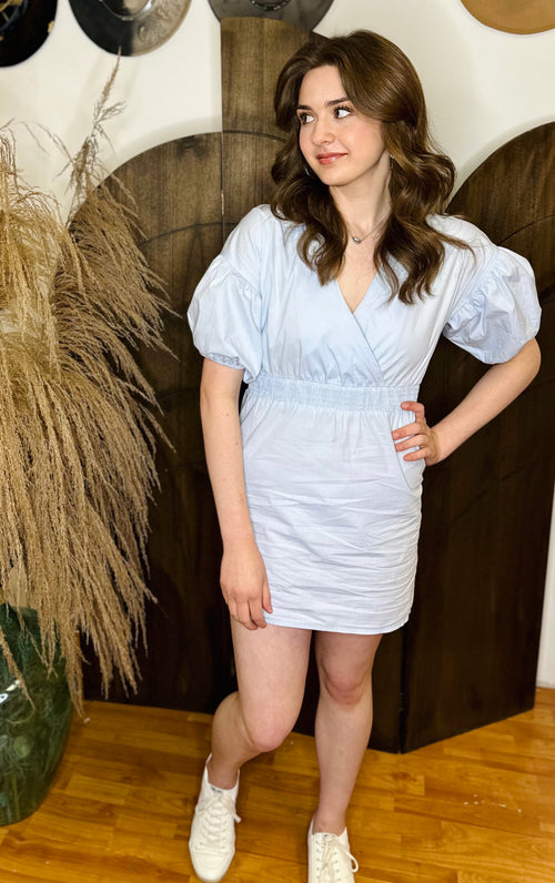 A light blue mini dress with short puffy sleeves, a cinched waist, and v neckline.