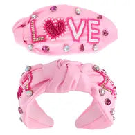 A light pink wide headband with beaded patches that say "love" on the sides. 