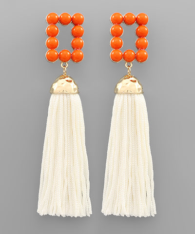 A pair of tassel earrings with bright orange detailing. 