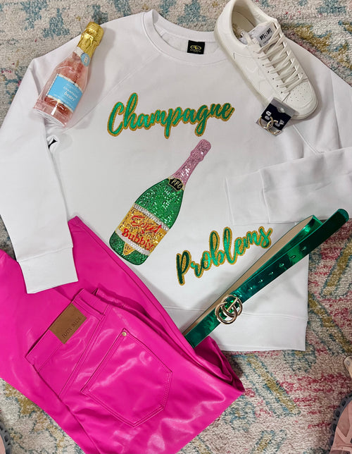 A white crewneck sweatshirt with "Champagne Problems" across the front in sequins along with a sequin bottle of champagne.