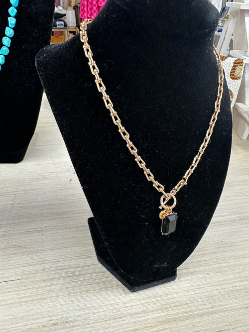 A gold chain necklace with a black crystal pendant.