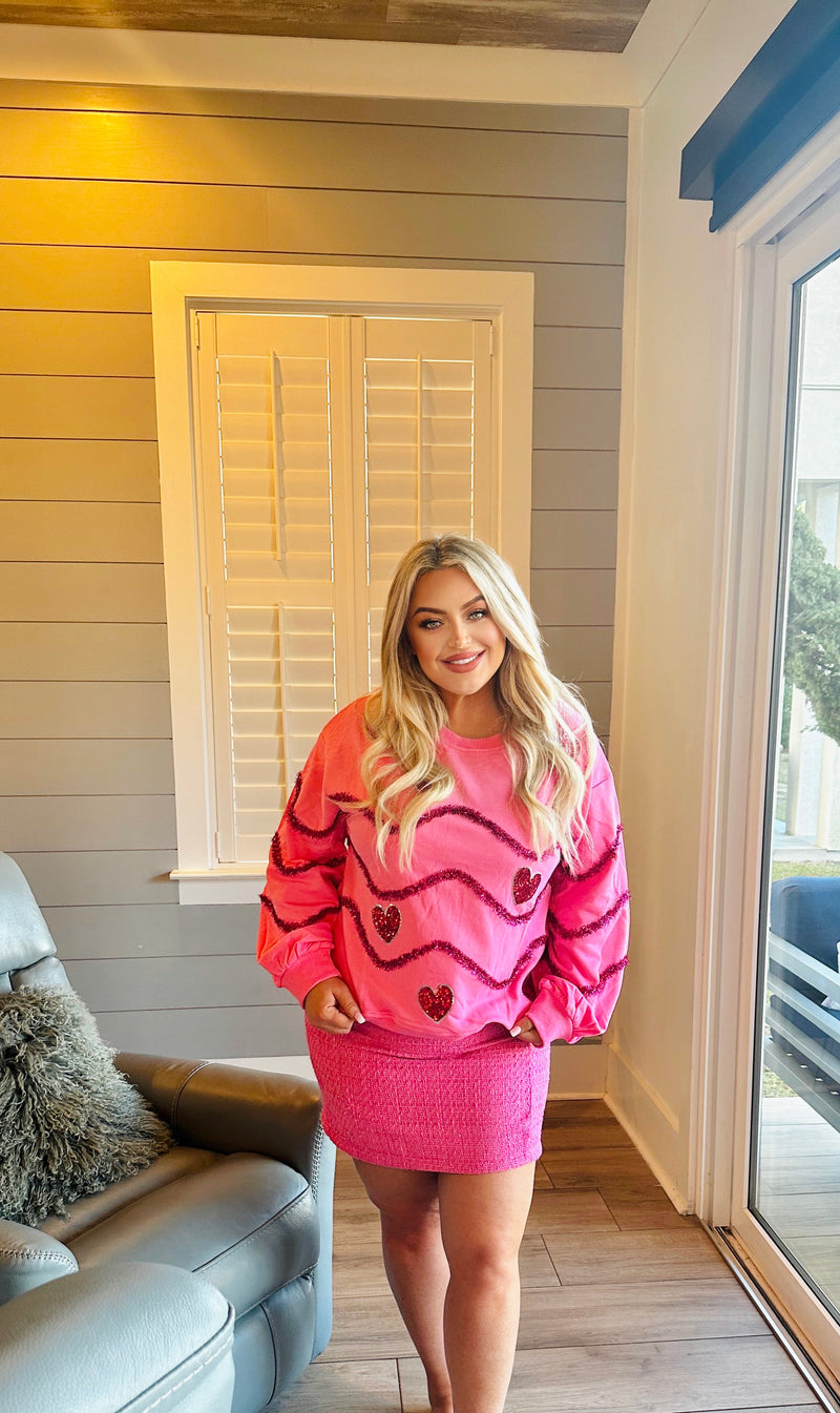 A hot pink oversized sweater with dark pink sequins in a wavy horizontal print and hearts on the front.