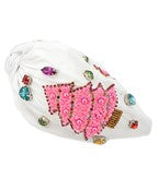A white wide headband with multicolored jewels and a pink christmas tree patch on the side.