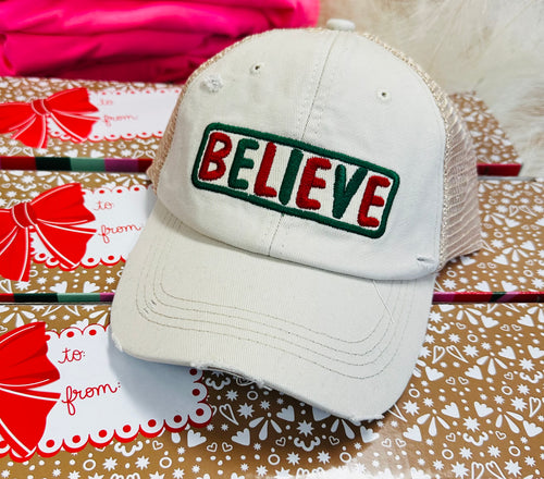 A white baseball cap with "Believe" written in red and green letters.
