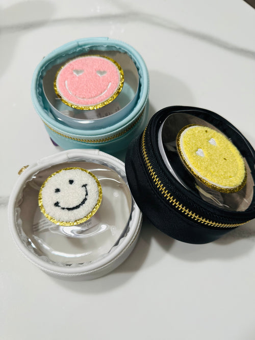 A travel jewelry case with a smiley face patch in the center.