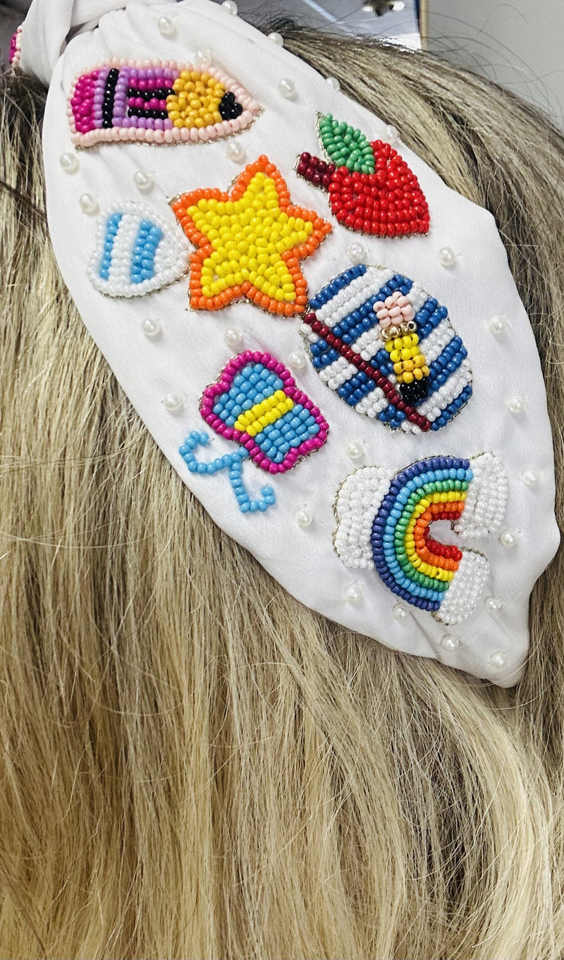 A white wide headband with school themed beaded patches throughout.