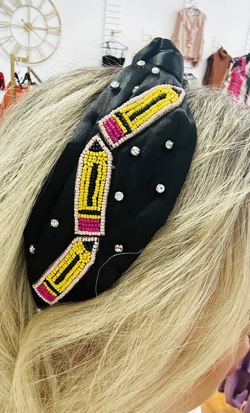 A black wide headband with beaded pencil patches on the sides.