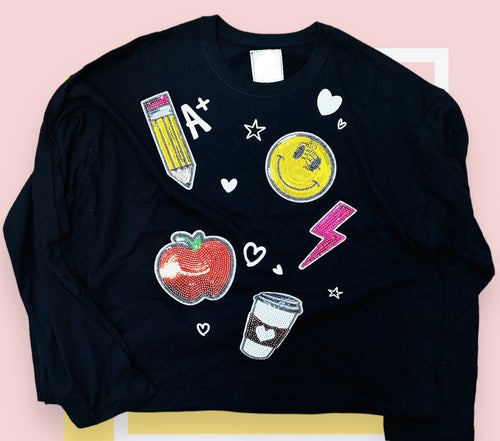 A black long sleeve t-shirt with sequin teacher themed patches featuring a pencil, smiley face, lightening bolt, apple, and coffee cup.