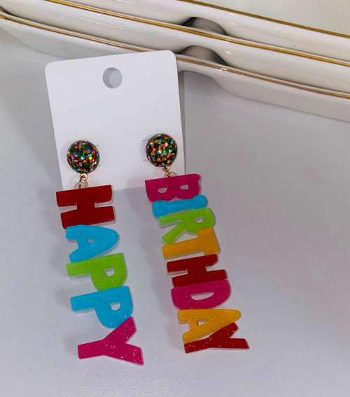 A pair of multicolored dangling earrings spelling out "Happy" on one and "birthday" on the other.