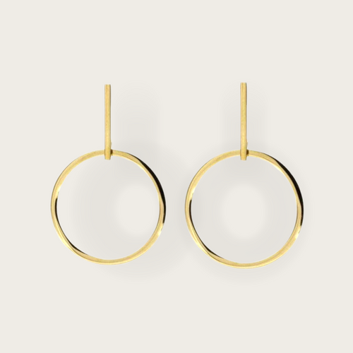 A pair of dangling gold earrings in a hollow circle shape. 