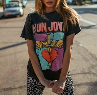 A graphic t-shirt with "Bon Jovi" written across the top in peach followed by a large graphic of a heart being pierced by a sword with angel wings.