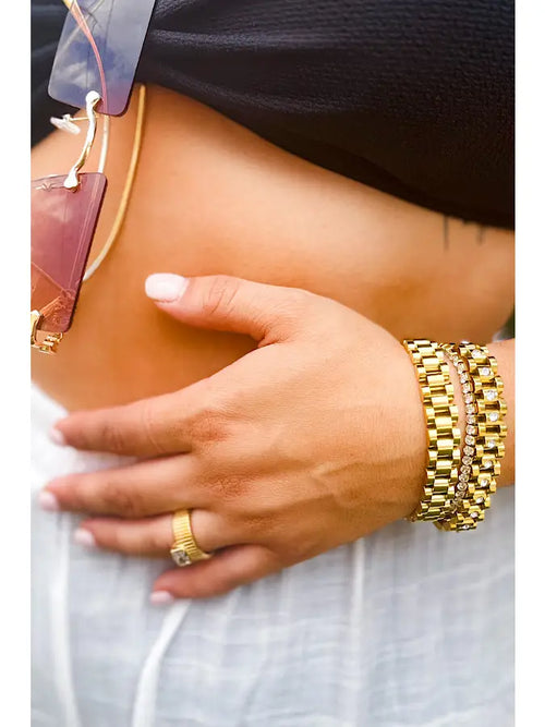 A chunky gold bracelet featuring a watch-link band and diamonds in the middle of the links.