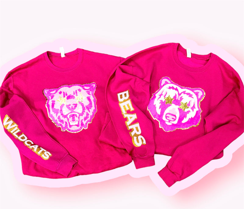 A hot pink crewneck sweatshirt with a mascot patch on the front and sleeve. 
