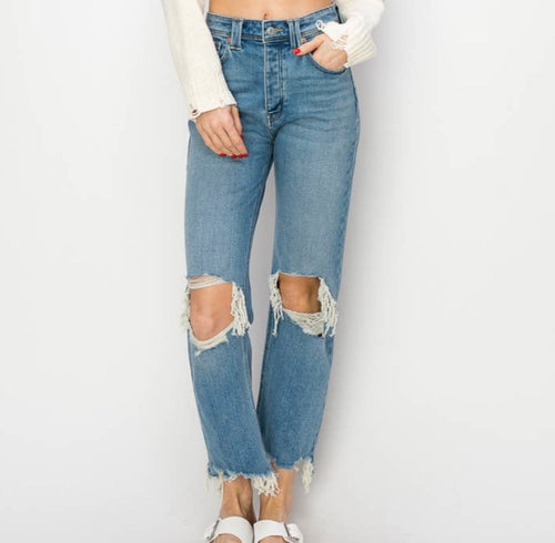 A pair of medium wash jeans with distressed holes in the knees, a high waist, and frayed hem. 