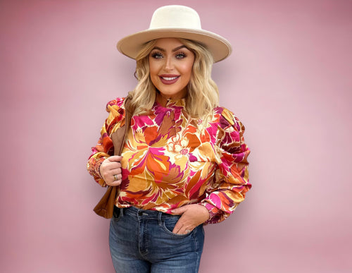 A tan, brown, and hot pink floral blouse with loose fit sleeves and a high neck.