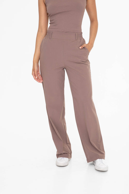 A pair of dark tan trousers with a wide leg, elastic waistband, and pockets.
