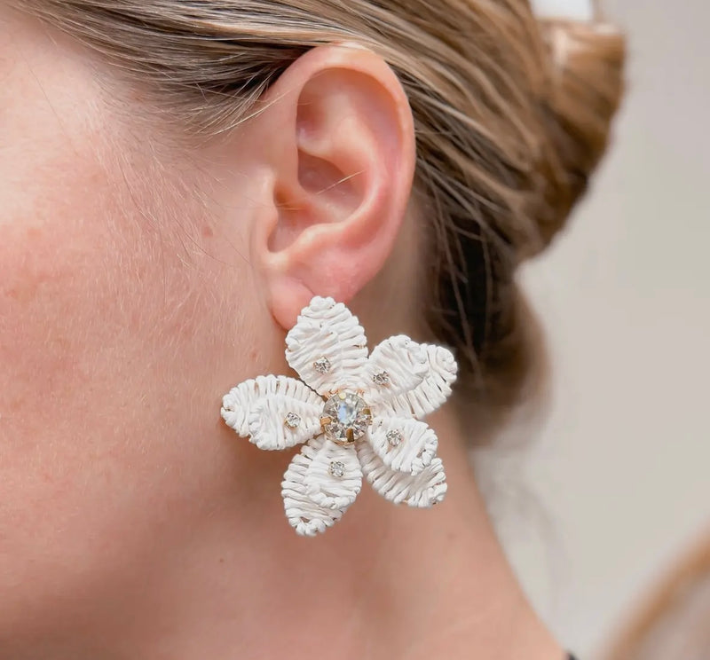 A pair of white dangling earrings in the shape of a flower and features rhinestones. 