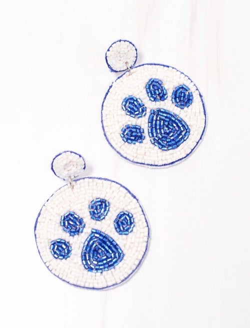 A pair of dangling earrings with beading in the shape of a white circle with a blue paw print in the center.