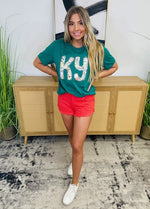 A dark turquoise t-shirt with "KY" on the front filled with a white, pink, and blue floral print inside the letters. 