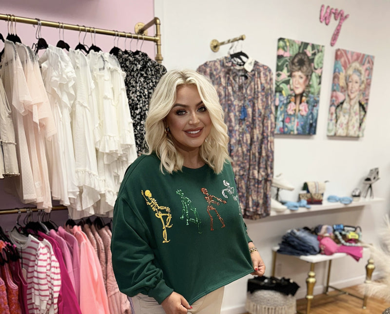 A dark green cropped crewneck sweatshirt with sequin dancing skeletons on the front. 