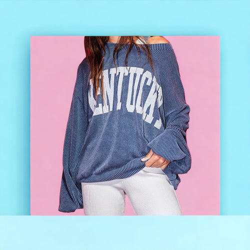 A wide neck, oversized blue ribbed crewneck with "Kentucky" written in large white letters. 