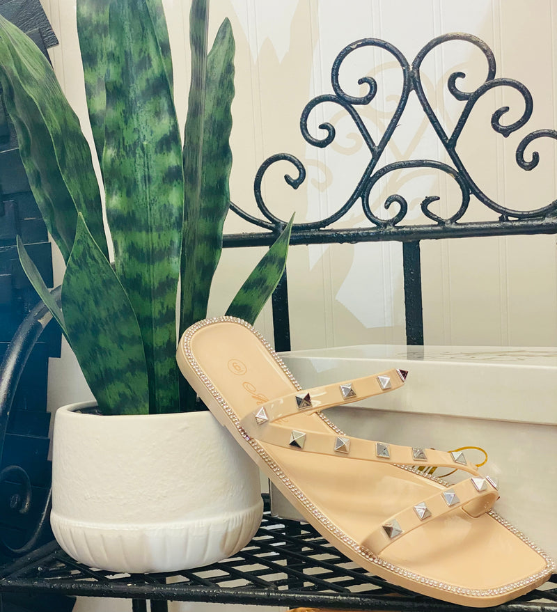 A pair of nude flat strappy sandals with silver studs on the straps and around the border of the shoe.